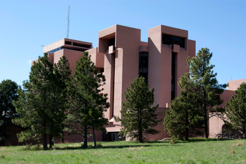 Exterior view of the NCAR Mesa Lab with pine trees, green grass, and blue sky.